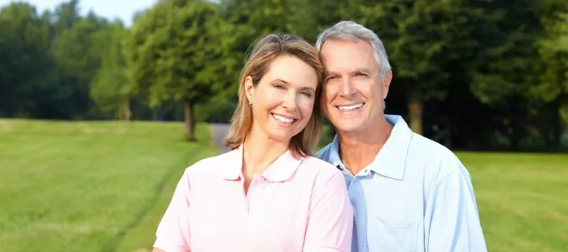Happy smiling middle-aged couple standing outdoors in a park, representing healthy family dental care.